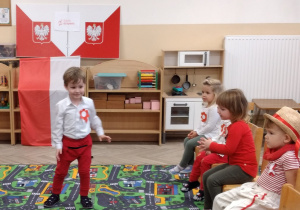 Chłopiec w białej koszuli i czerwonych spodniach prezentuje swój strój.