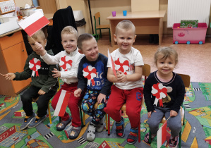 Dzieci siedzą z flagą w rączkach.
