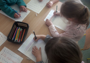Dzieci ćwiczą rękę podczas pisania szlaczków.