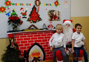 Dwoje dzieci siedzi na kolanach Mikołaja.