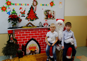 Dwoje dzieci siedzi na kolanach Mikołaja.