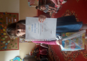 Dziewczynka trzyma dyplom i nagrodę.