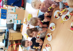 Dzieci sporządzają szaszłyki owocowe.