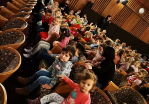 Dzieci siedzą na krzesłach w teatrze i czekają na spektakl.