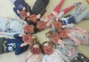 Dzieci leżą w maskach na dywanie.