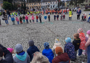Dzieci świętują Dzień Przedszkolaka na placu, tańcząc i śpiewając.