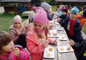 Dzieci jedzą pieczone w ognisku ziemniaki z kiszoną kapustą.