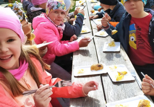 Dzieci jedzą pieczone w ognisku ziemniaki z kiszoną kapustą.