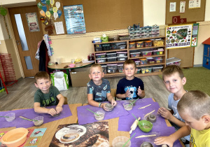 Dzieci siedzą przy stoliku i lepią z gliny.