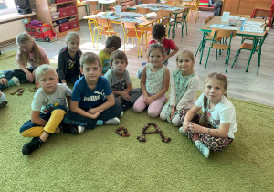 Dzieci siedzą na dywanie i układają literkę a z kasztanów.