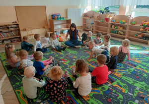 Dzieci siedzą na dywanie i uczą się przez zabawę języka angielskiego.