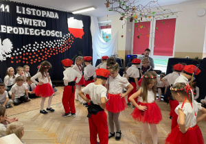 Dzieci w biało - czerwonych strojach tańczą Krakowiaka.