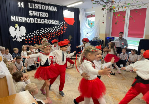 Dzieci w biało - czerwonych strojach tańczą Krakowiaka.