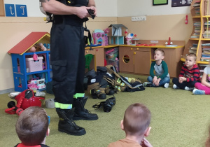Strażak prowadzi pogadankę dla dzieci pokazując sprzęt strażacki