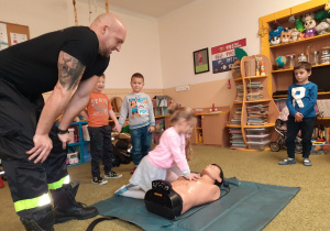 Dzieci uczą się wykwalifikowanej pierwszej pomocy pod nadzorem strażaka.