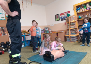 Dzieci uczą się wykwalifikowanej pierwszej pomocy pod nadzorem strażaka.