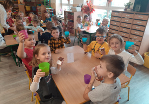 Dzieci przy stolikach piję zdrowie misia z kubeczkami w ręku z soczkiem.