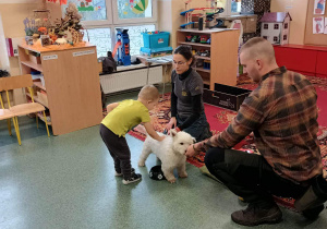 Dziecko karmi psa przy współpracy opiekunów.