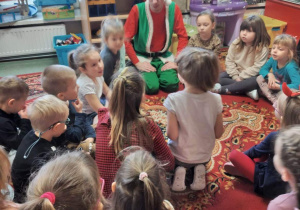 Dzieci siedzą na dywanie i rozmawiają z Elfem.