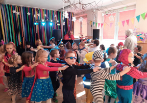 Dzieci w przebraniach tańczą na balu karnawałowym.