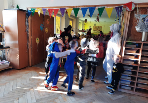 Dzieci w przebraniach tańczą na balu karnawałowym.