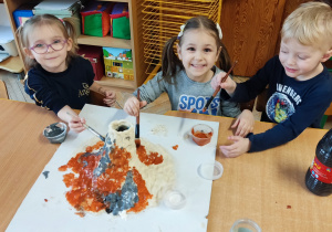 Dzieci siedzą przy stoliku i budują wulkan.