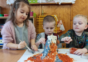 Dzieci siedzą przy stoliku i budują wulkan.