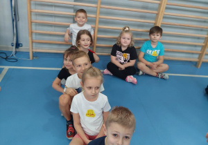 Dzieci w strojach gimnastycznych siedzą po turecku.