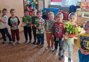 Chłopcy stają z kwiatami dla dziewczynek z okazji Dnia kobiet.