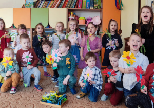 Dzieci pozują do zdjęcia z kwiatami w rękach.