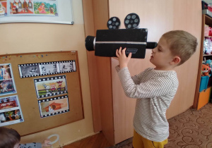 Chłopiec bawi się zrobioną ze styropianu kamerą.
