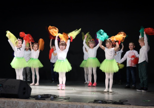 Dziewczynki w zielonych spódniczkach tańczą taniec z chusteczkami.