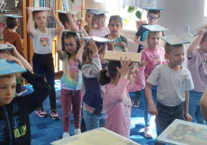 Dzieci w bibliotece chodzą z książkami na głowie.