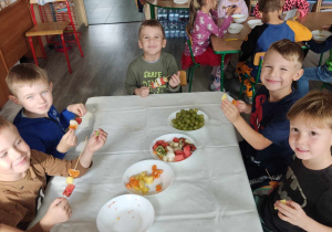 Dzieci siedzą przy stole pełnym owoców.