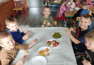 Dzieci siedzą przy stole pełnym owoców.