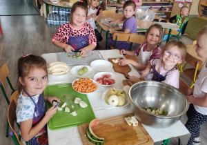 Dzieci przy stoliku kroją owoce na deskach.