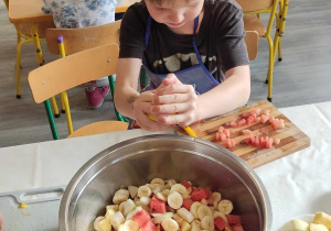 Chłopiec przed miską pełną pokrojonych owoców.
