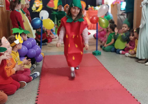 Dziewczynka przebrana za truskawkę idzie po czerwonym dywanie.