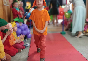 Chłopiec przebrany za marchewkę idzie po czerwonym dywanie.