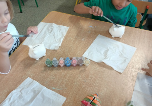 Dzieci malują gliniane skarbonki.