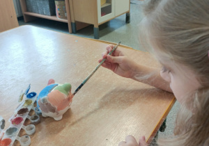 Dzieci malują gliniane skarbonki.